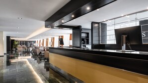 Un moderno vestíbulo de hotel con una elegante recepción negra y dorada, pisos de mármol y mobiliario contemporáneo.