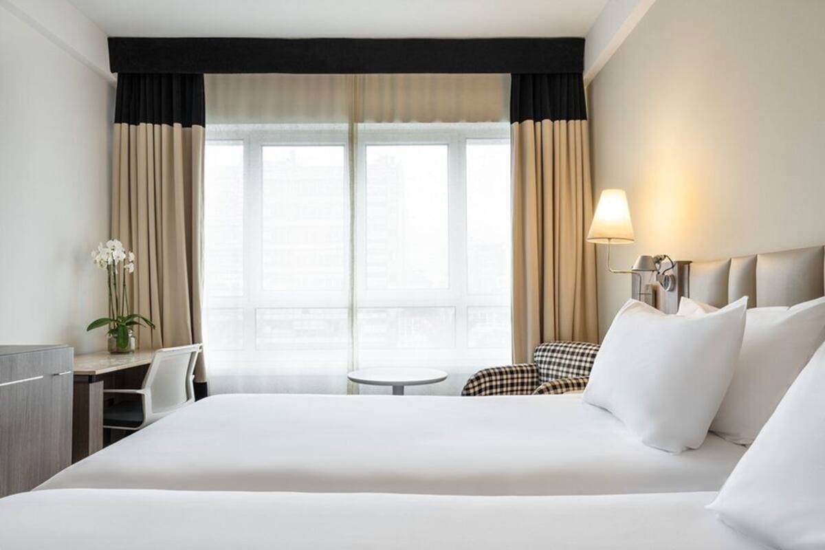Ein Hotelzimmer mit einem großen Bett, einem Schreibtisch, einem Sessel, einem kleinen Tisch und einer Lampe.