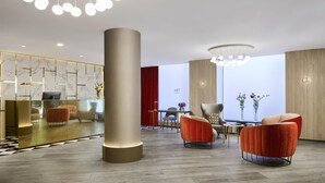 A modern lobby with a large reception desk, seating area, and decorative lighting. - NH Madrid Balboa (Madrid)