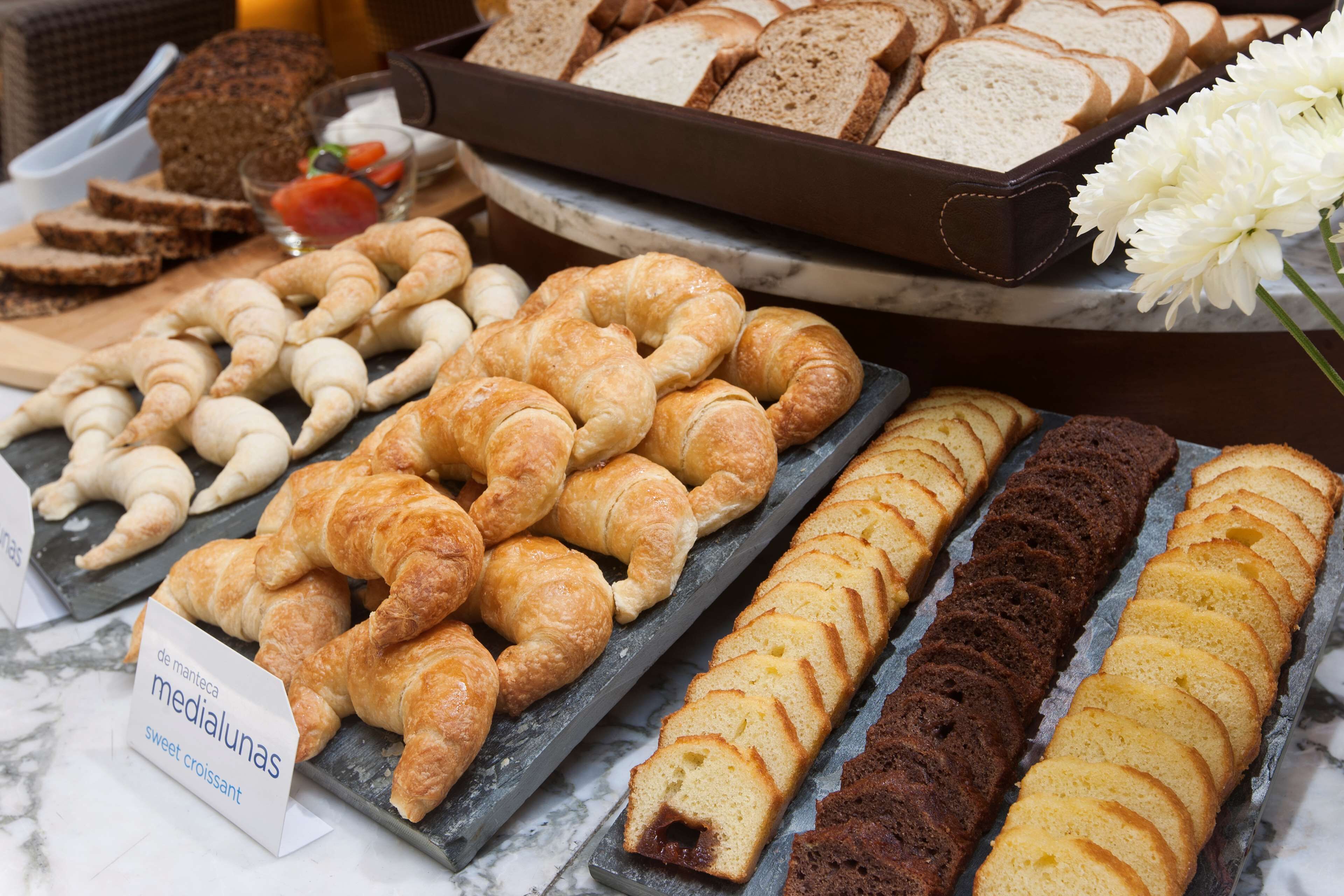 Une variété de viennoiseries et de pains, ainsi qu’un gâteau, présentés sur un comptoir en marbre.