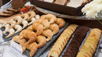 Une variété de viennoiseries et de pains, ainsi qu’un gâteau, présentés sur un comptoir en marbre.