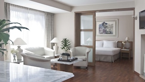 Une chambre d’hôtel moderne, équipée d’un lit, de deux fauteuils, d’une table basse et d’une grande fenêtre avec des rideaux.