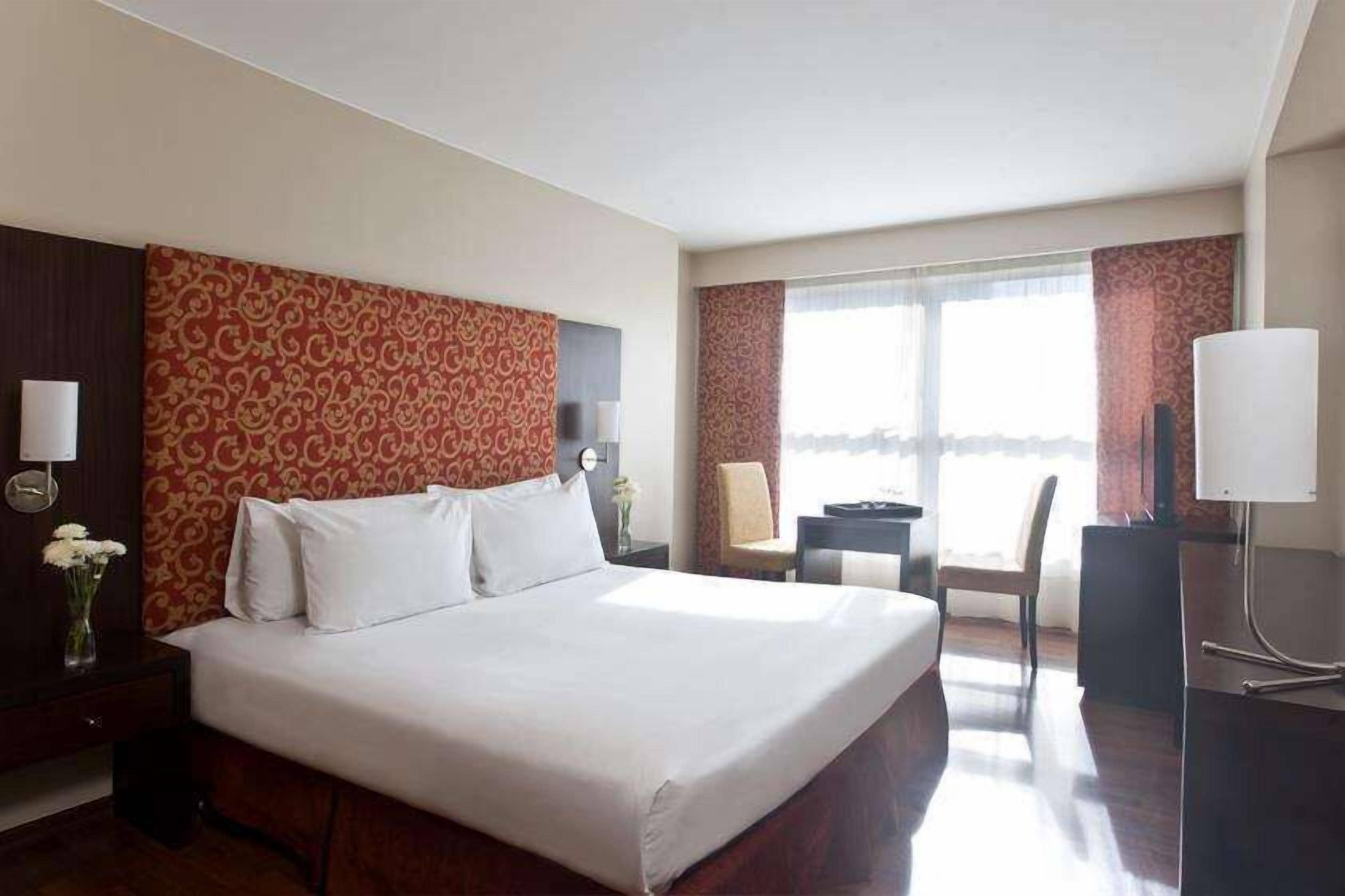 Ein Hotelzimmer mit einem großen Bett, einem Schreibtisch, einem Sessel und einem Fernseher.