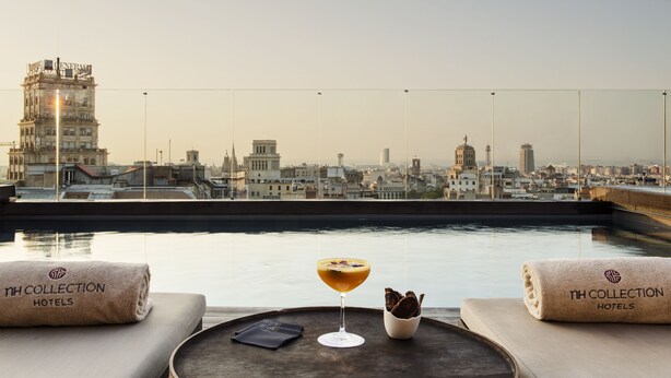 Terraço no telhado com vista para a cidade, um cocktail em um suporte e toalhas com a marca do hotel.