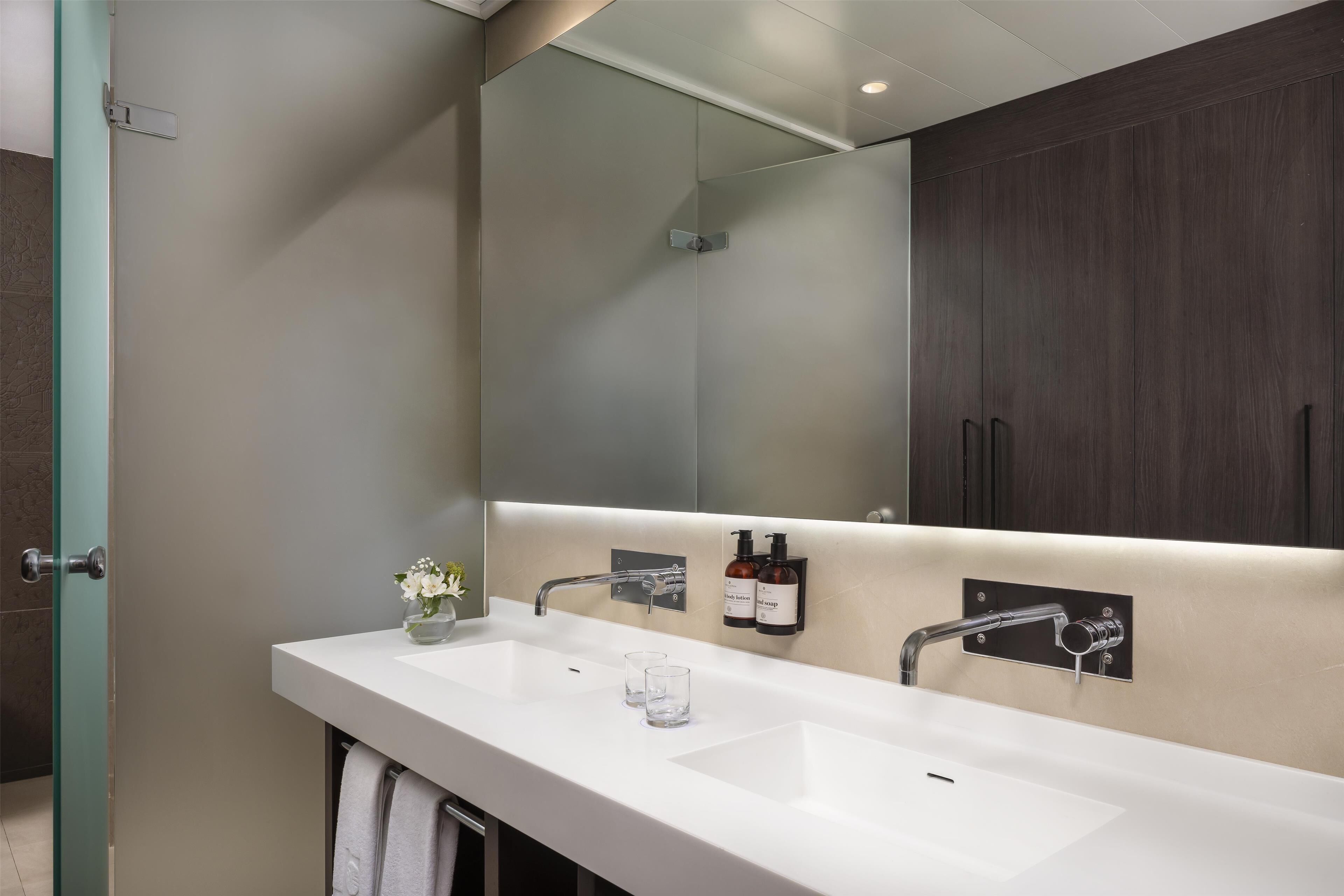 A modern bathroom with a white sink, two faucets, a mirror, and a towel rack.