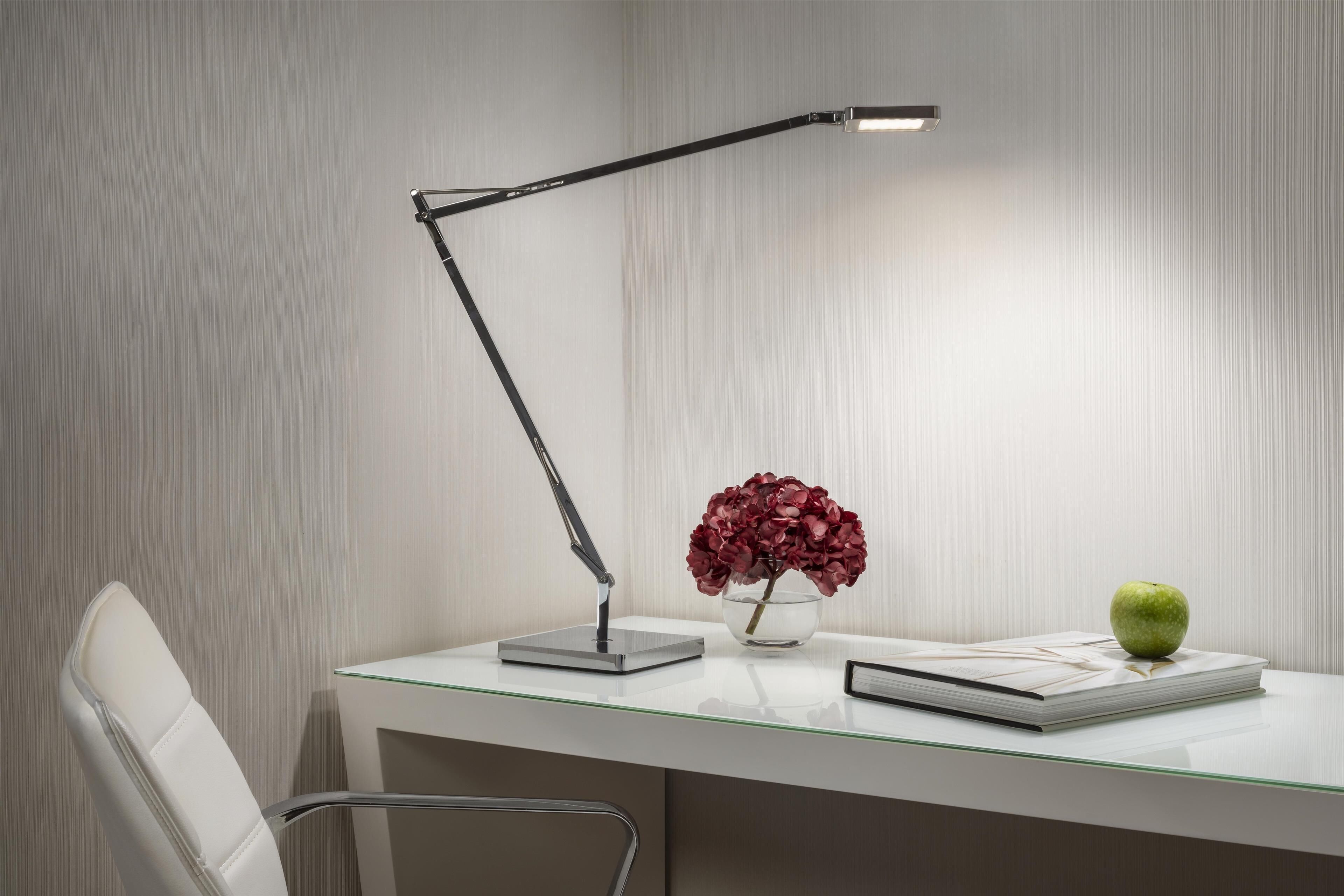 A modern desk with a lamp, a vase with flowers, and an apple.