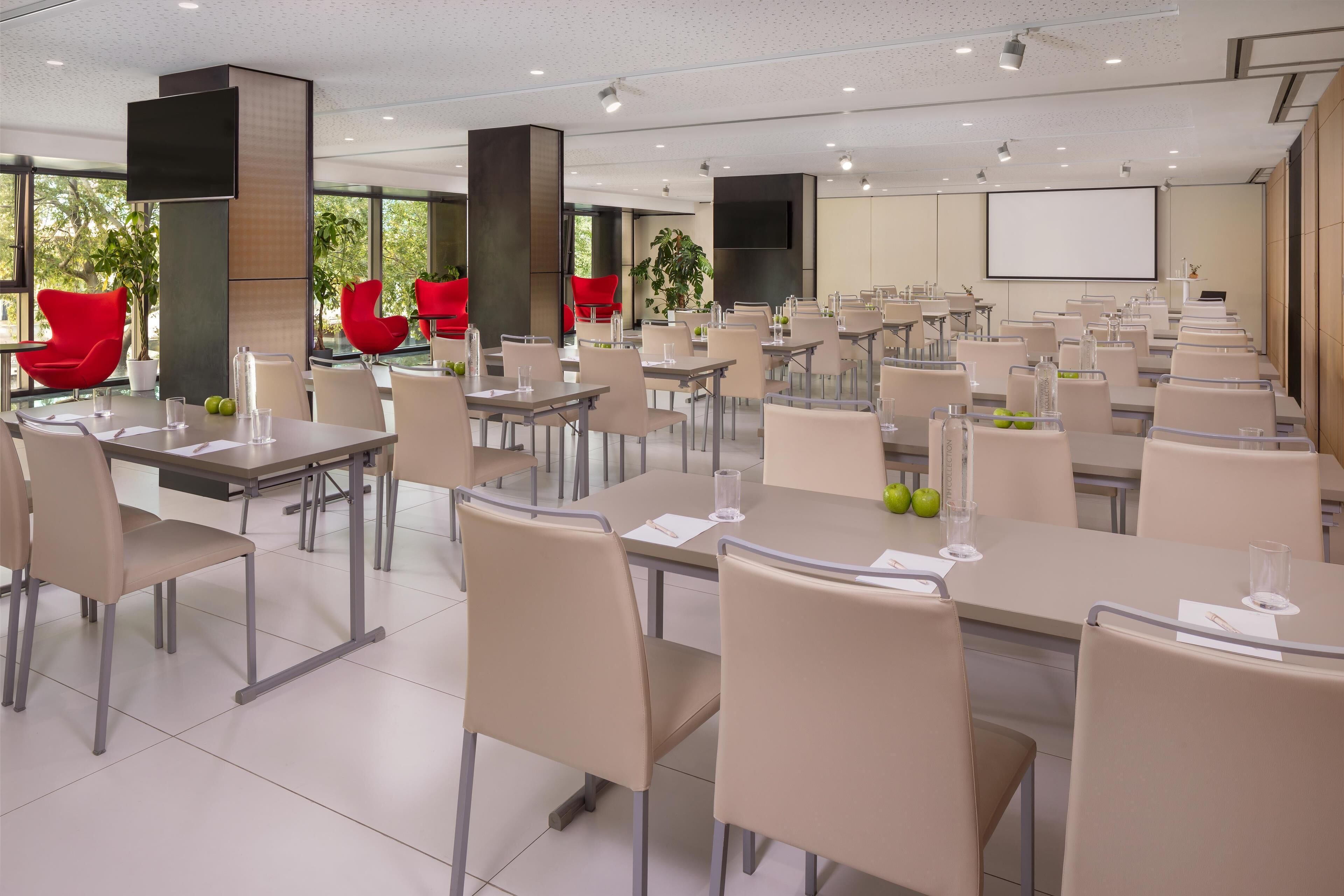 A modern conference room with multiple tables and chairs, large screens, and a projector.