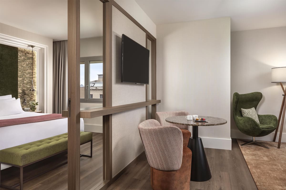 A hotel room with a bed, a desk, a chair, a TV, and a lamp.