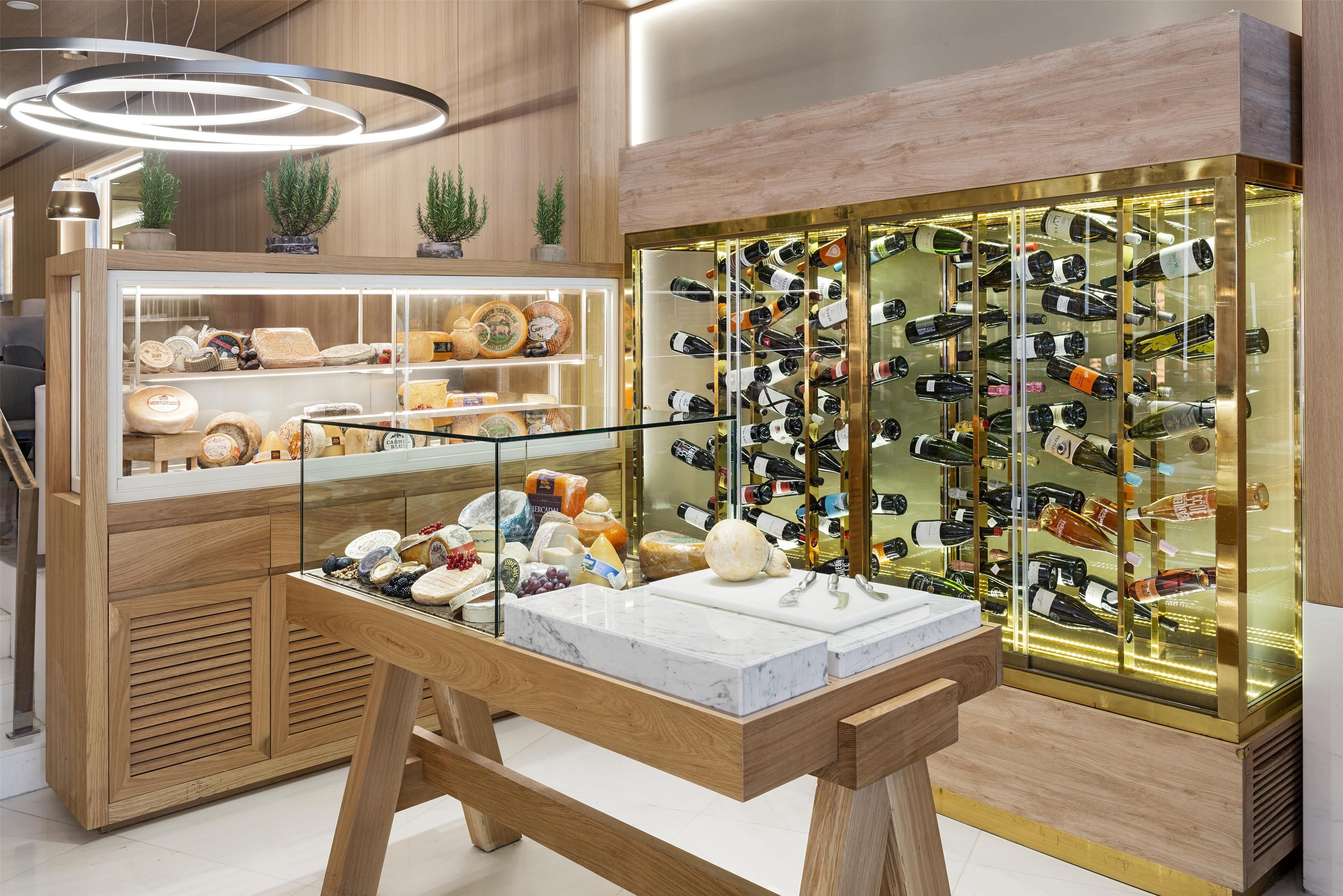 Exhibición de quesos y vinos con mostrador de mármol y botellero de vidrio.