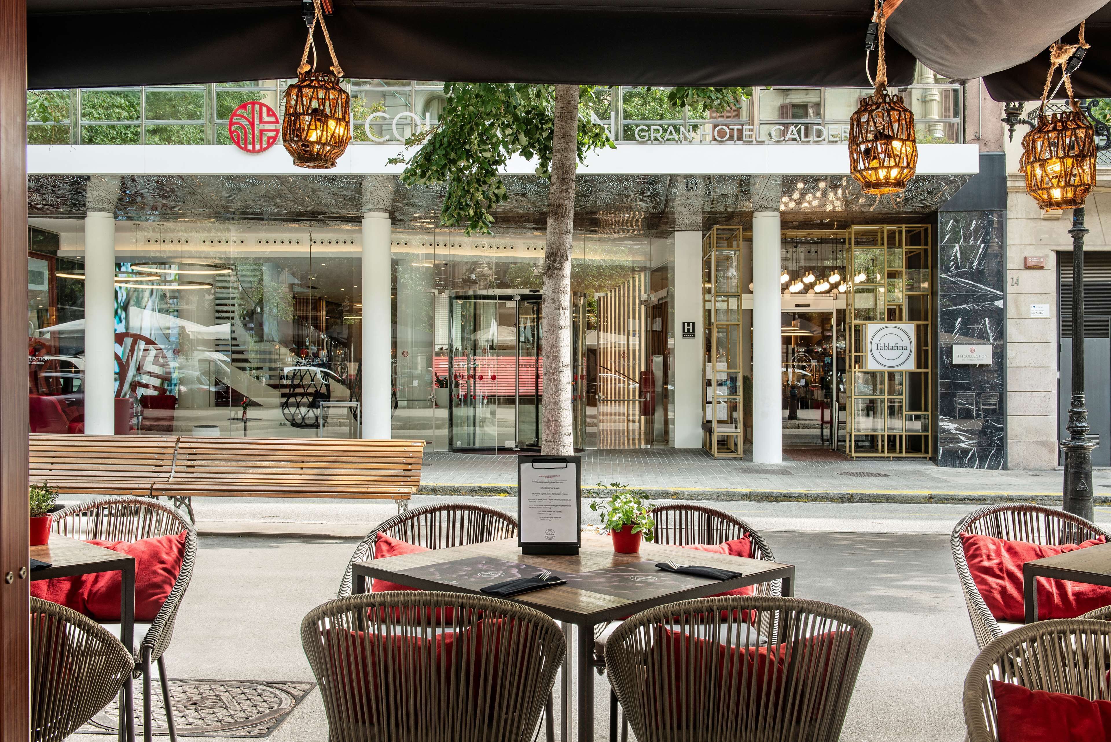 An outdoor seating area with wicker chairs and tables, a menu stand, and a view of a building with a sign that reads "GRAND HOTEL CALLE."