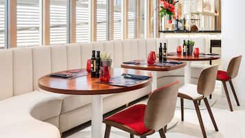 Un espace repas moderne avec des tables rondes, des sièges confortables et une vue sur la ville grâce à de grandes fenêtres.