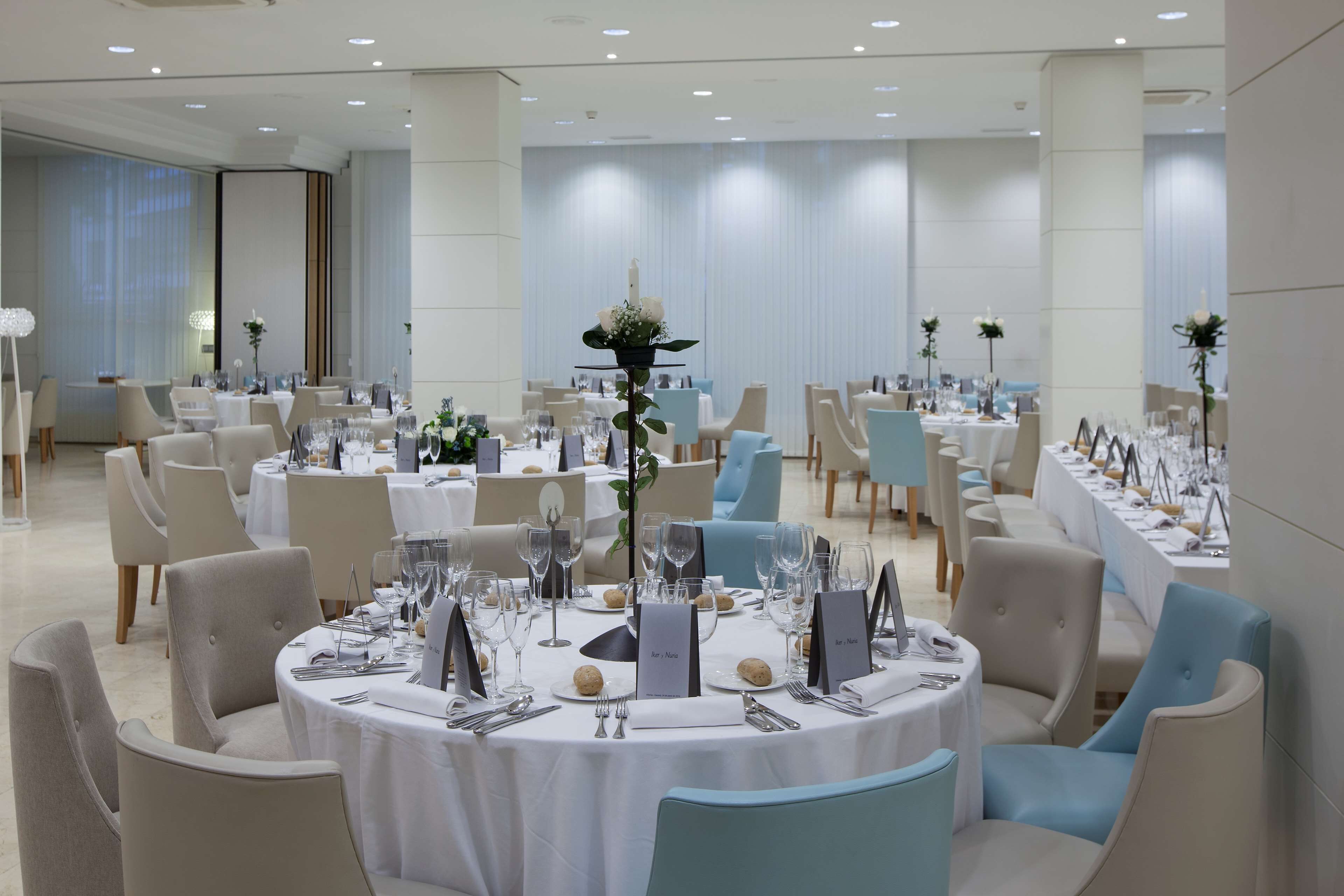 Un salón de banquetes con mesas redondas dispuestas para cenar, cada una con individuales y centros de mesa florales.