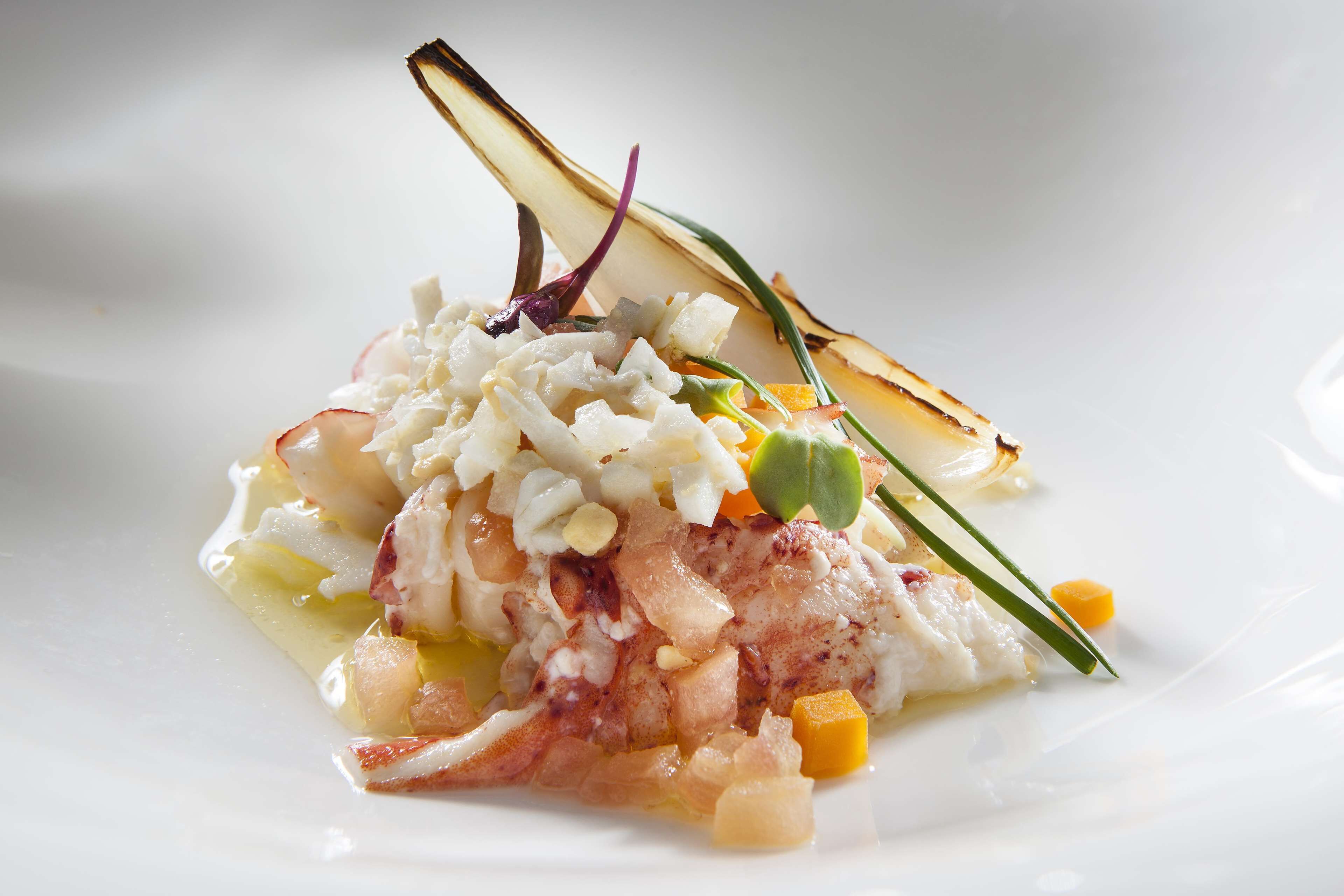 Un plato con mariscos, verduras y una guarnición sobre una vajilla blanca.