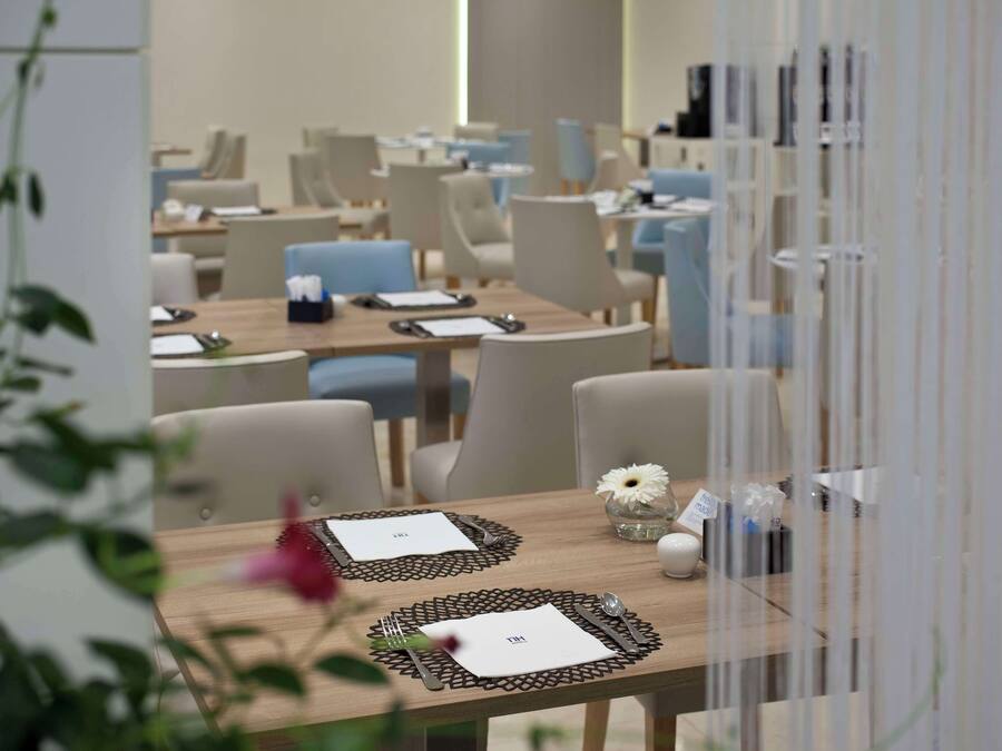 Un área de comedor con mesas dispuestas para dos comensales, cada una con un mantel individual, cubiertos y un pequeño jarrón con una flor.