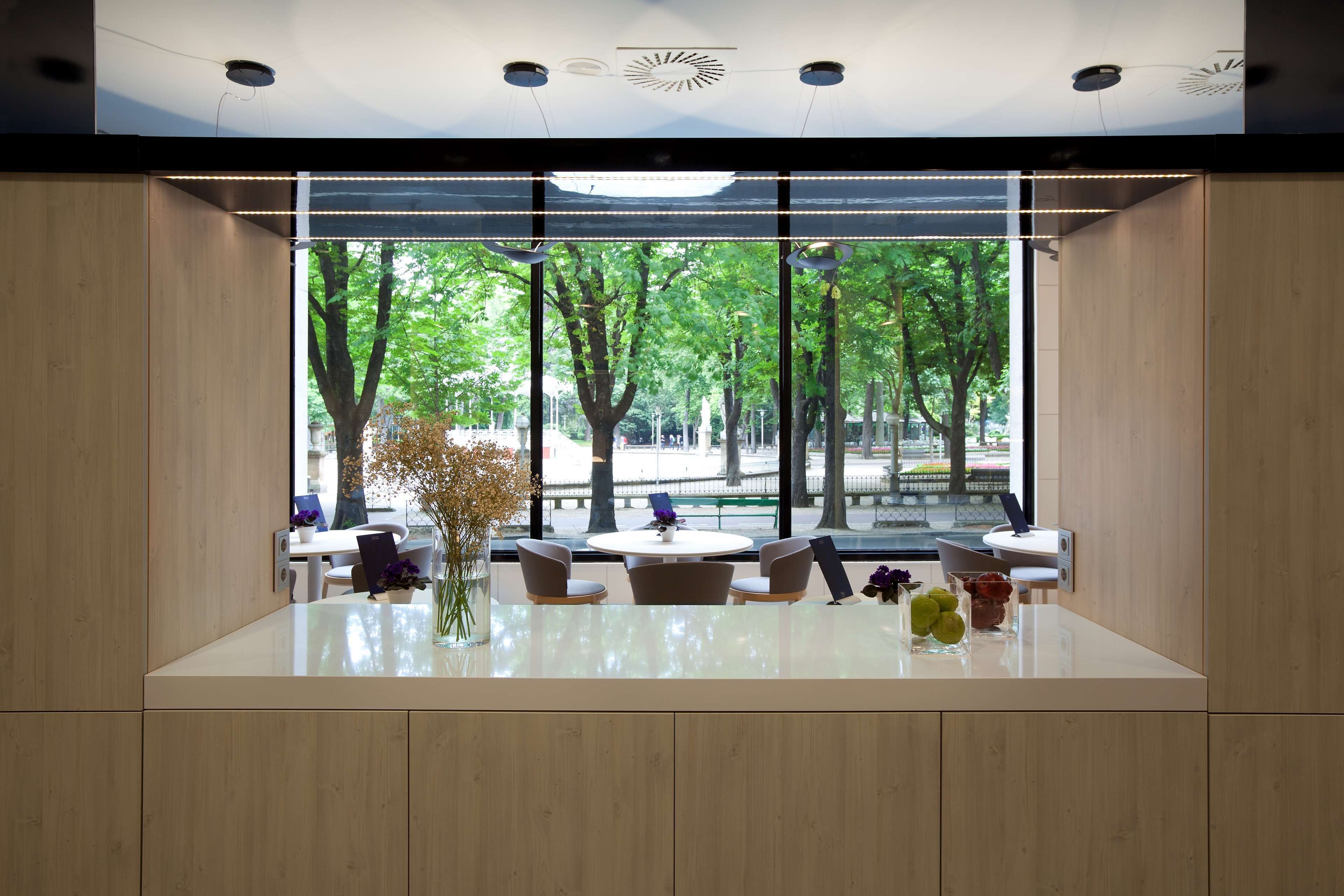 Un intérieur moderne avec une table centrale, des chaises et une vue sur les arbres à travers de grandes fenêtres.