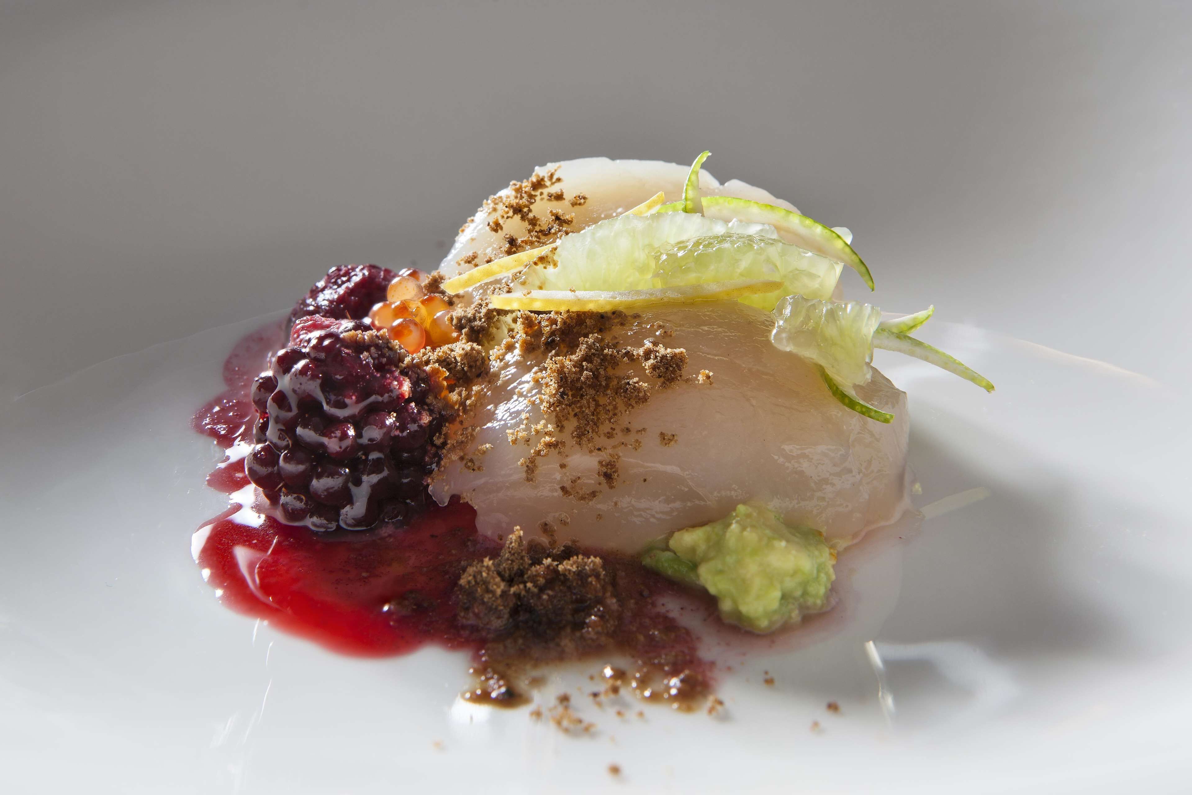 Plat blanc amb un plat que consisteix en un aliment translúcid en capes, decorat amb una fulla verda, una compota de baies i un cruixent marró.