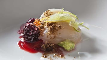 Plat blanc amb un plat que consisteix en un aliment translúcid en capes, decorat amb una fulla verda, una compota de baies i un cruixent marró.