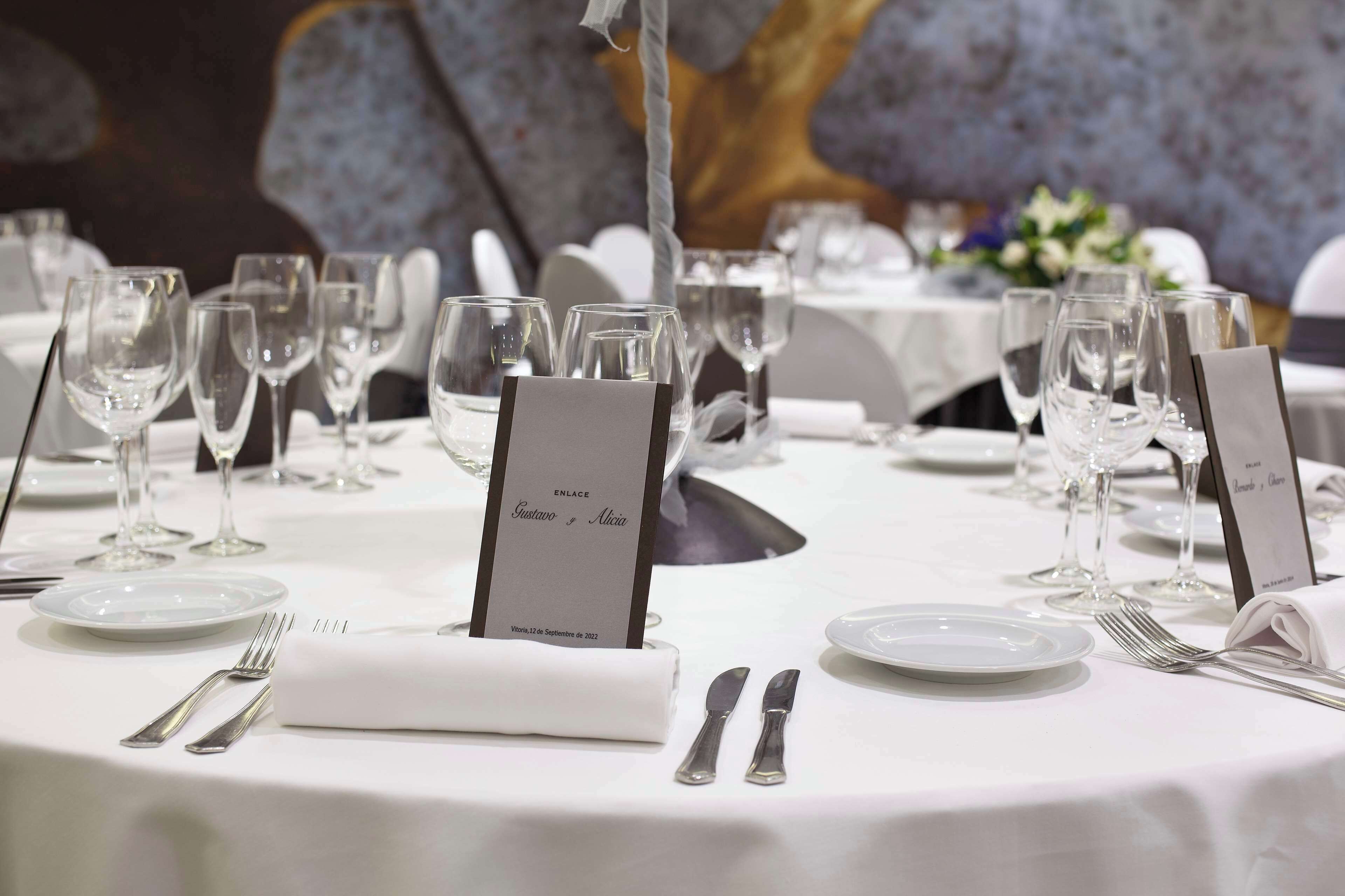 Una mesa dispuesta para un evento formal, con un atril para el menú, copas de vino y cubiertos.