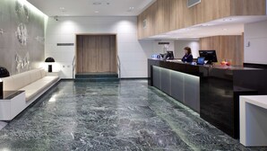 Un área de recepción moderna con suelo de mármol, mostrador de recepción, puerta de madera y un rincón de estar con sofá.