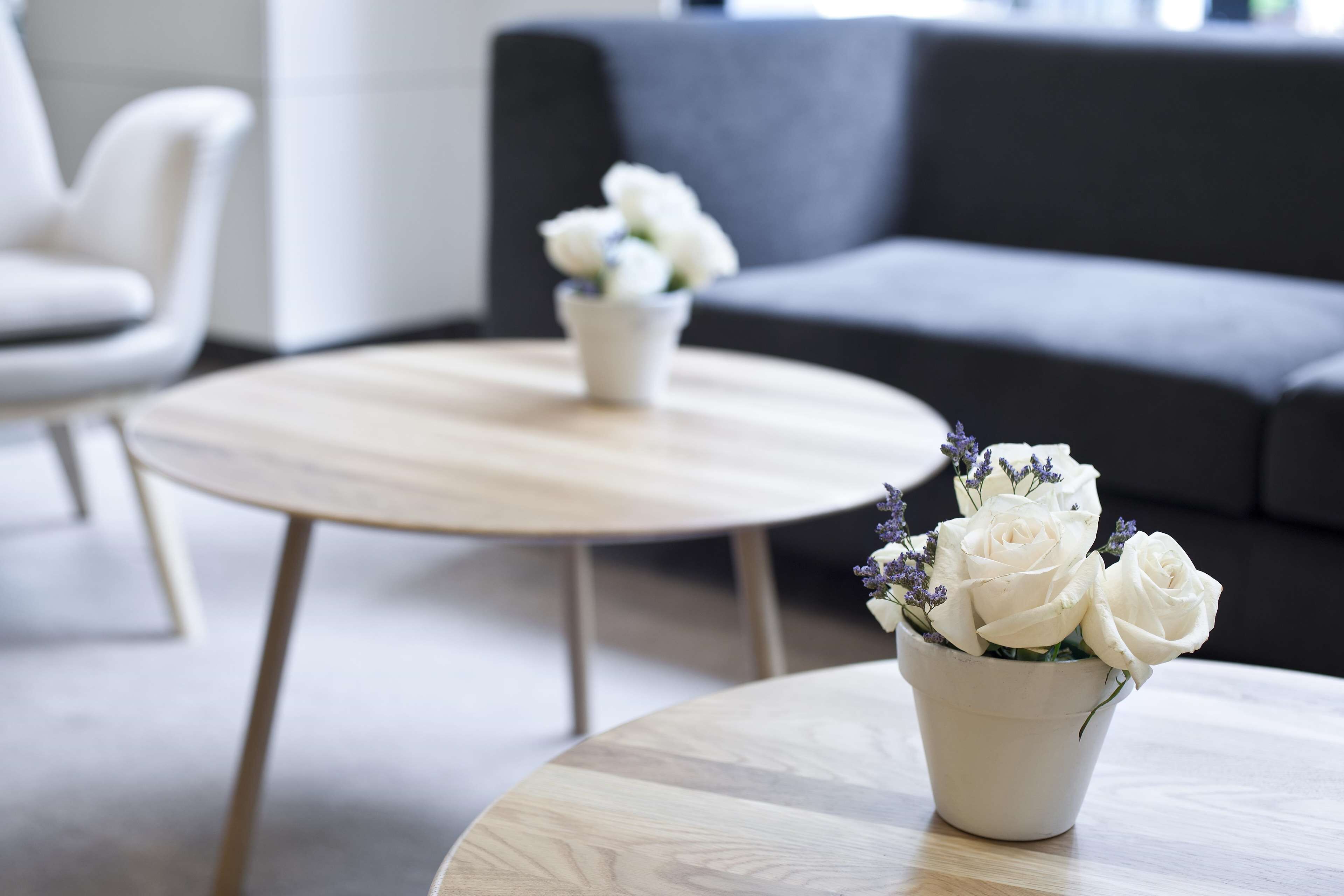 Un salón moderno con una mesa de centro redonda de madera y un jarrón blanco con flores blancas.