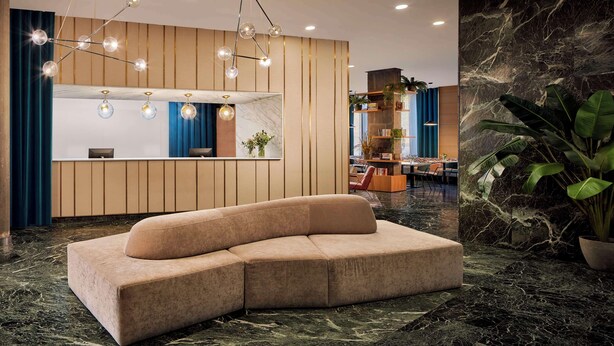 A modern lobby with a curved sofa, a reception desk, and a large mirror. - NH Ciudad de Cuenca (Cuenca)