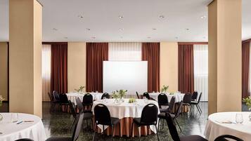 A conference room with round tables, black chairs, and a large white screen.