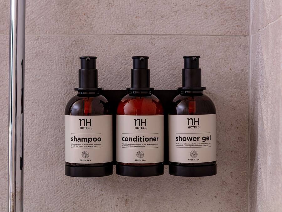 Drie flesjes hoteltoiletartikelen (shampoo, conditioner, douchegel) op een muur.