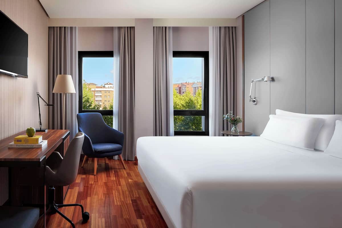 A hotel room with a large bed, a desk with a chair, a TV, and a window with curtains.