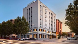 A modern hotel building with a prominent "NH Hotels" sign, multiple floors, and a corner location with trees and parked cars. - NH Ciudad de Cuenca (Cuenca)
