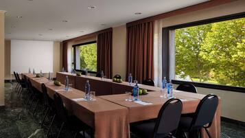 Un salón de conferencias con una mesa larga, sillas y vistas a árboles a través de amplias ventanas.