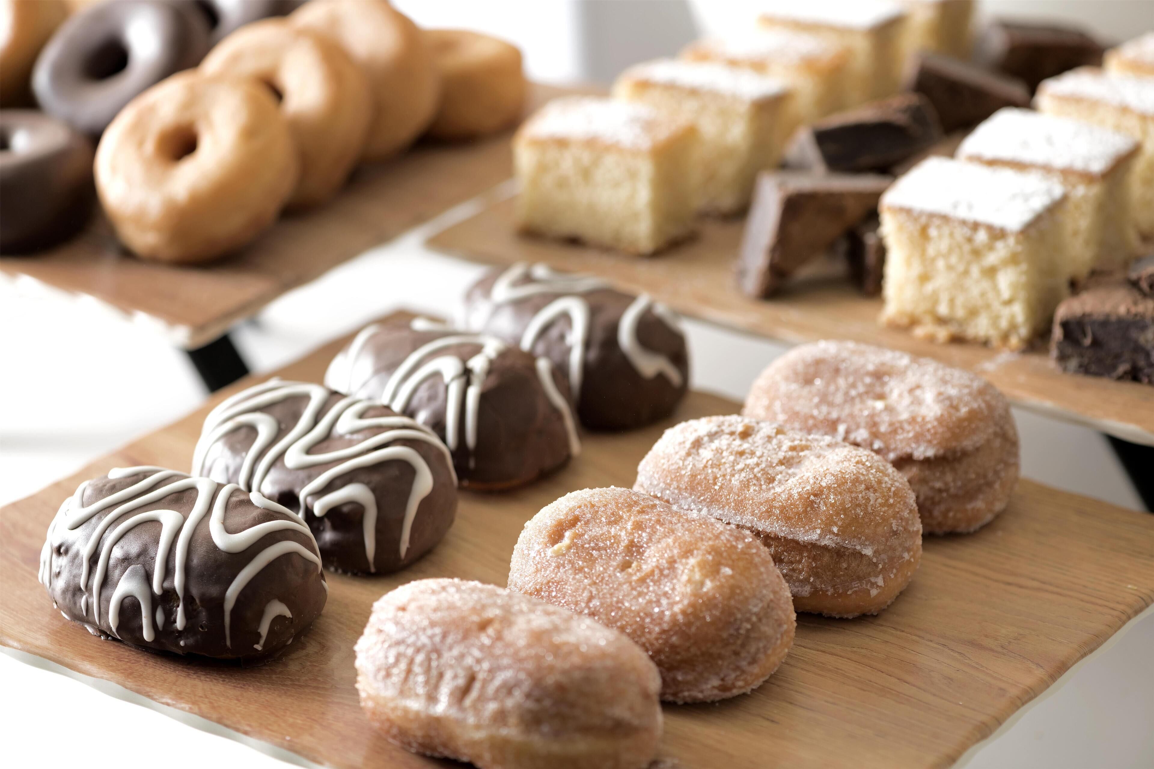 Diversas pastas en tablas de madera, incluyendo rosquillas cubiertas de chocolate y espolvoreadas con azúcar.