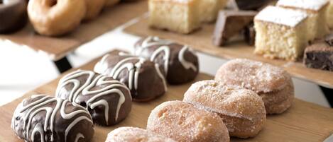 Diversas pastas en tablas de madera, incluyendo rosquillas cubiertas de chocolate y espolvoreadas con azúcar.
