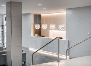 Una zona de recepción moderna con mostrador de mármol, barandales metálicos e iluminación colgante única.