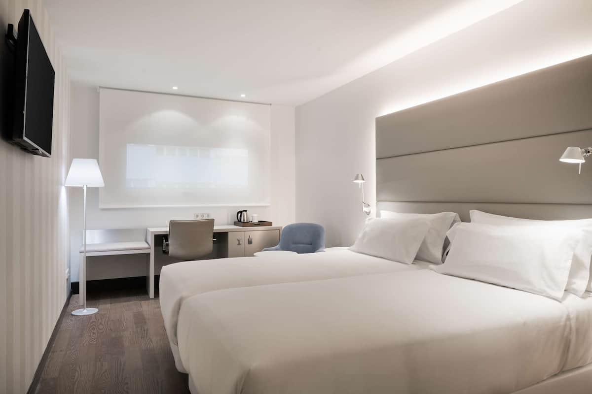 A hotel room with two beds, a desk, a chair, a flat-screen TV, and a projector screen.