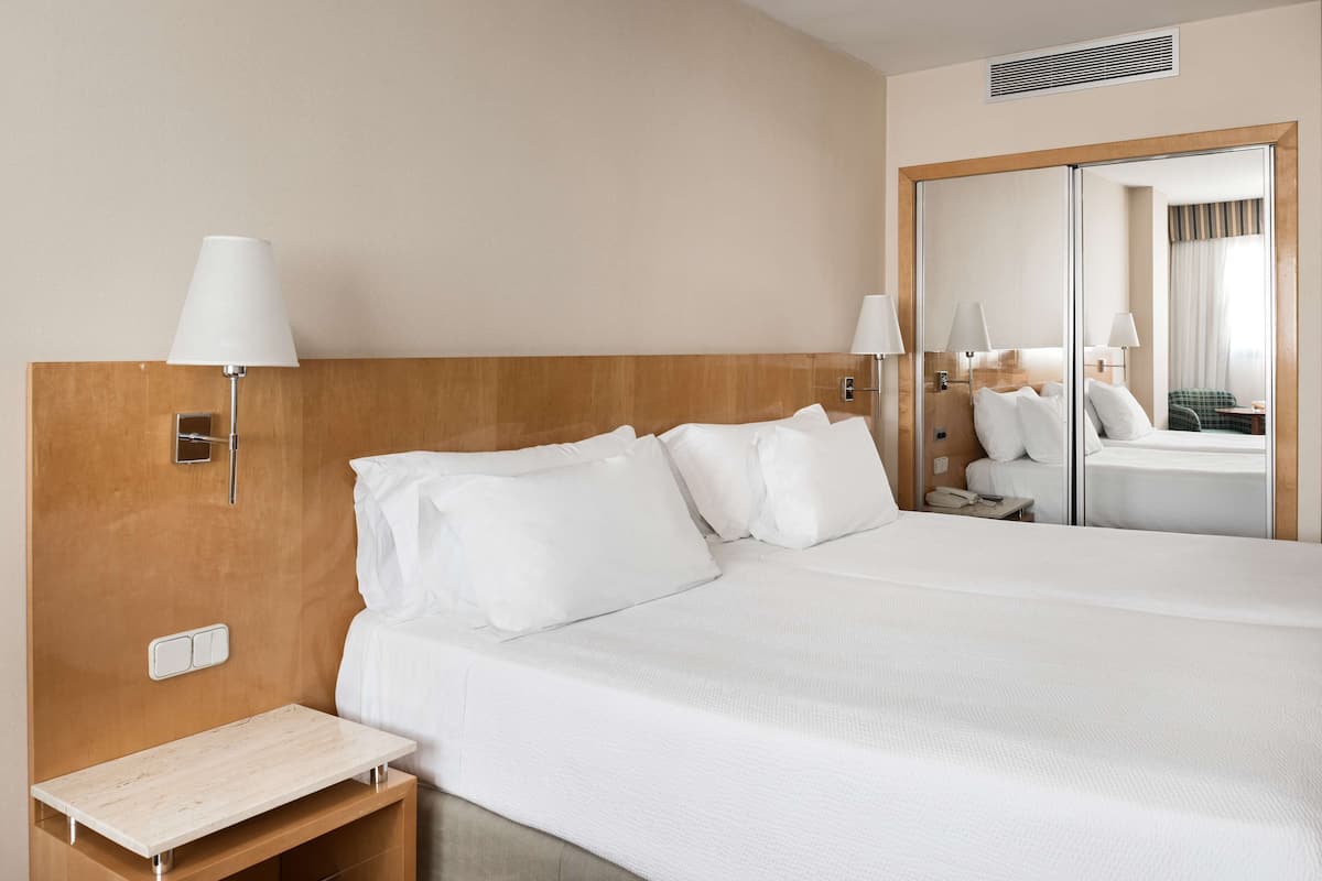 A hotel room with a large bed, a bedside table, a mirror, and a wall-mounted lamp.