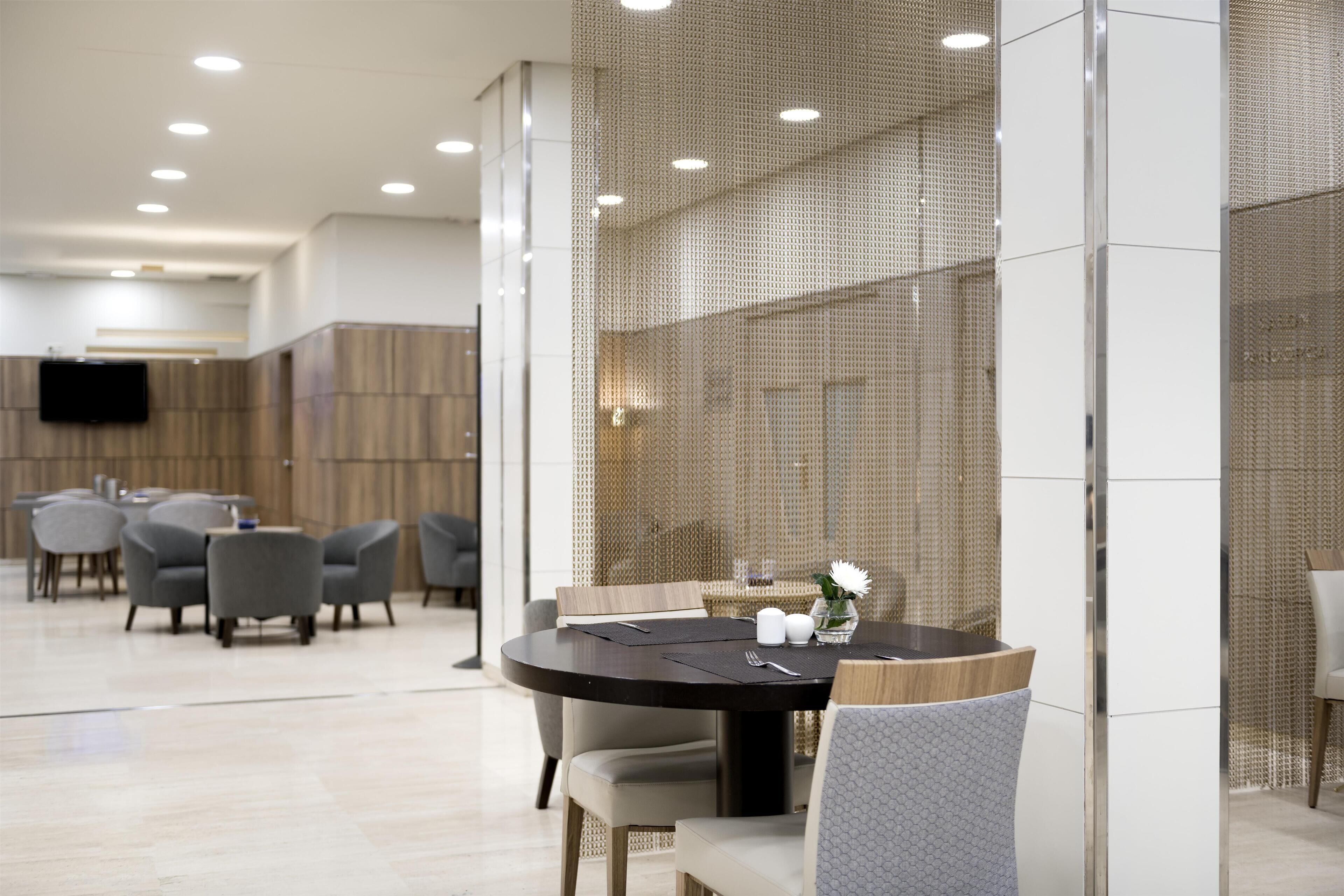A modern dining area with round tables, grey upholstered chairs, and a decorative vase on the table.