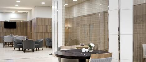 A modern dining area with round tables, grey upholstered chairs, and a decorative vase on the table.