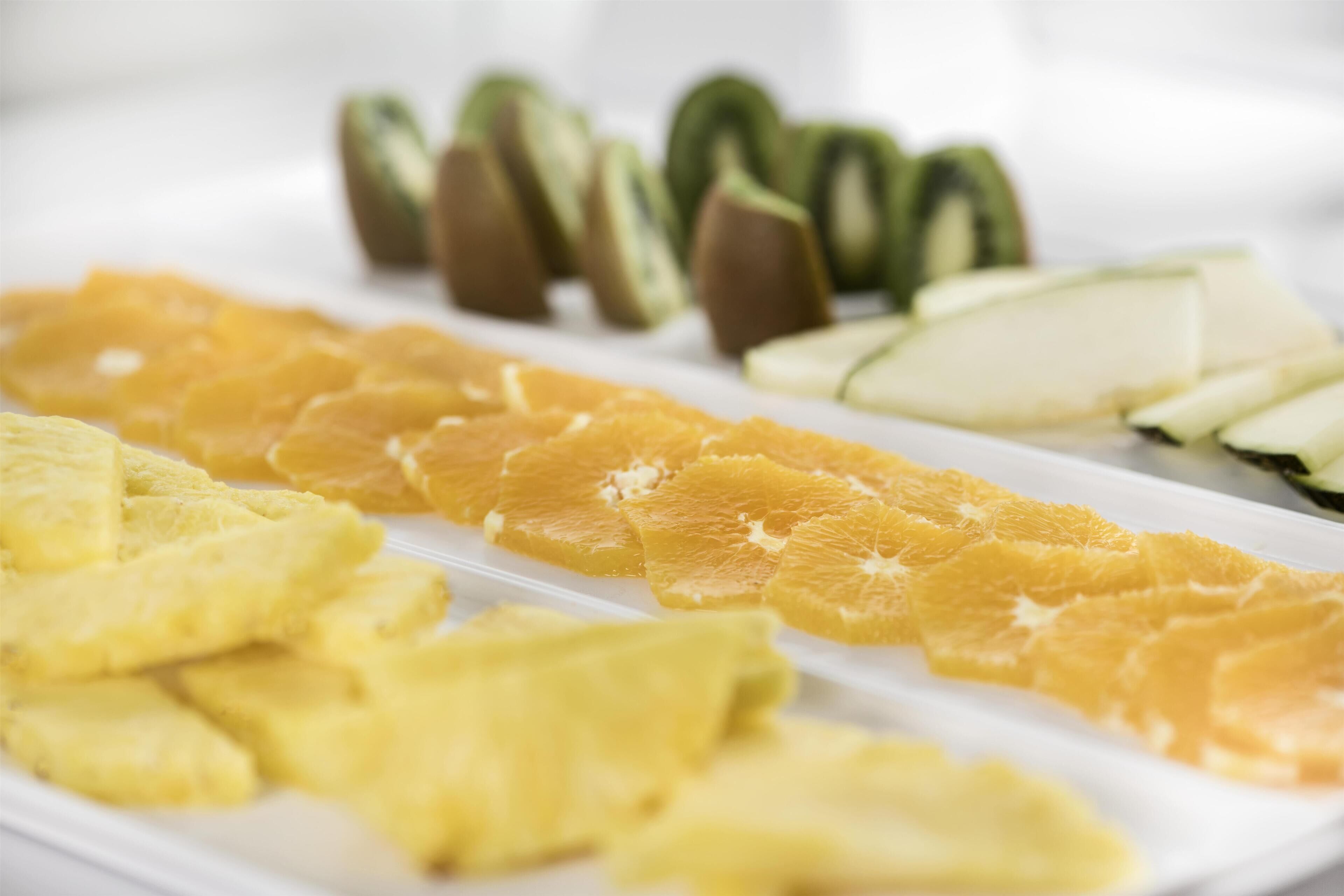 Une assiette blanche contenant des fruits coupés en tranches, notamment des oranges, des kiwis et des ananas.
