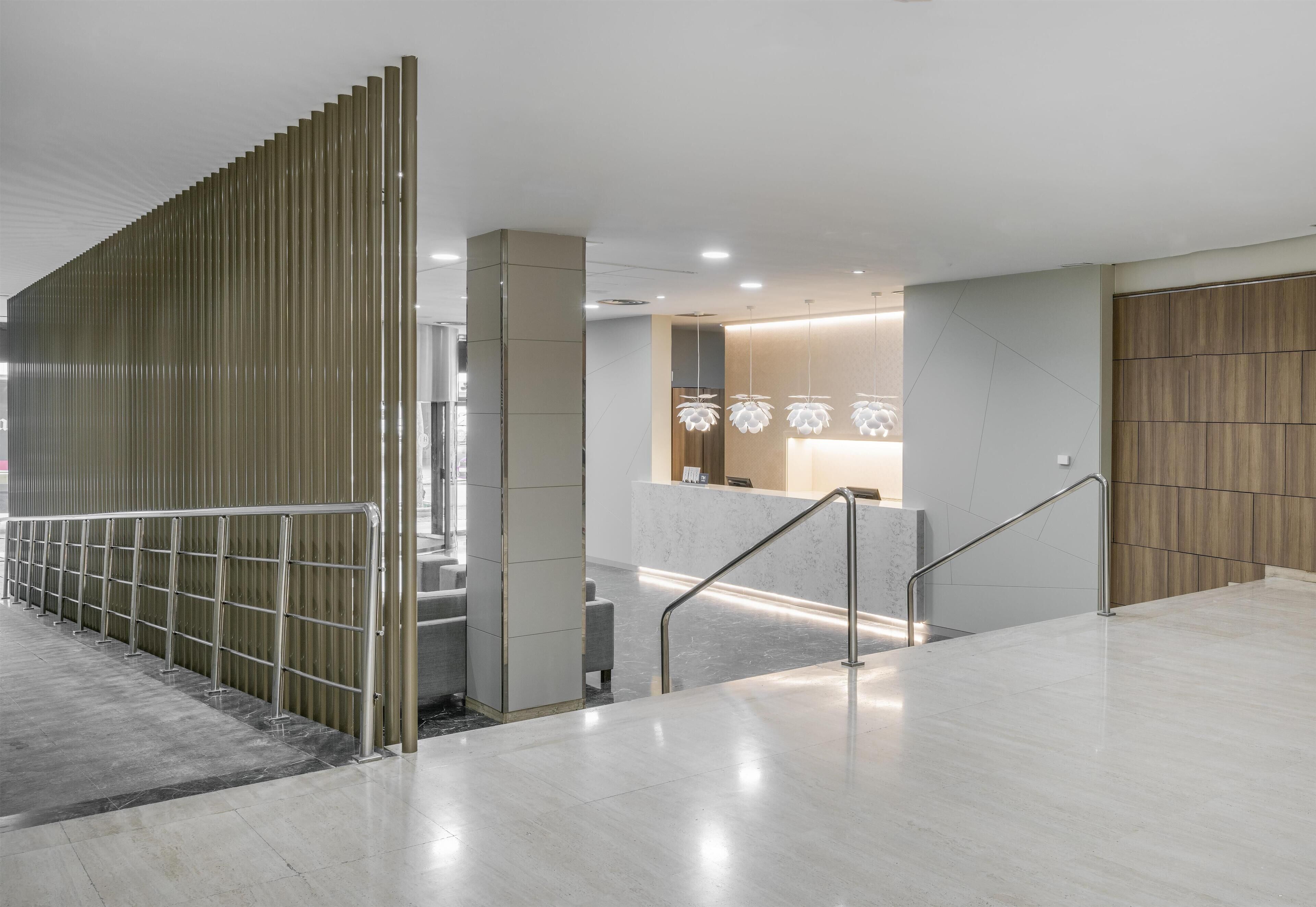 Un moderno vestíbulo de hotel con piso de mármol, una mesa de recepción y un separador de madera.