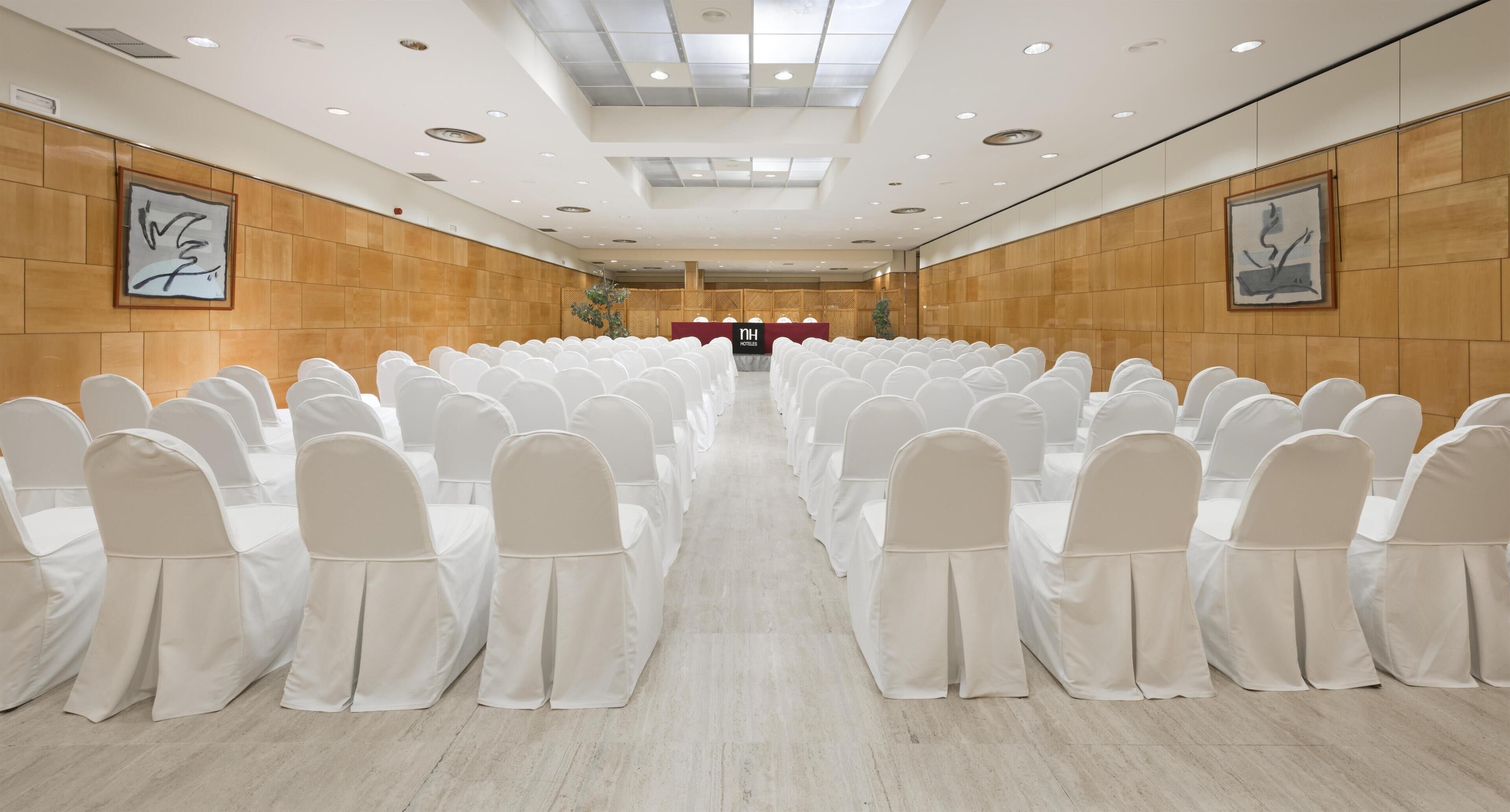 A conference room with rows of white chairs and tables, a podium, and framed artwork on the walls.