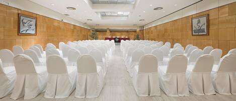 A conference room with rows of white chairs and tables, a podium, and framed artwork on the walls.
