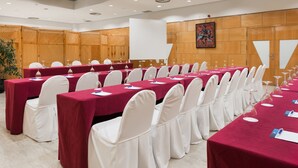 A conference room with multiple tables covered in red tablecloths, white chairs with white covers, and a wooden partition wall with a framed artwork. - NH Ciudad Real (Ciudad Real)