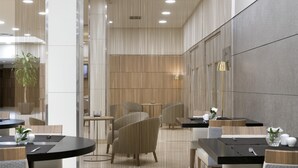 A modern dining area with round tables, wicker chairs, and a decorative wall with a perforated pattern. - NH Ciudad Real (Ciudad Real)