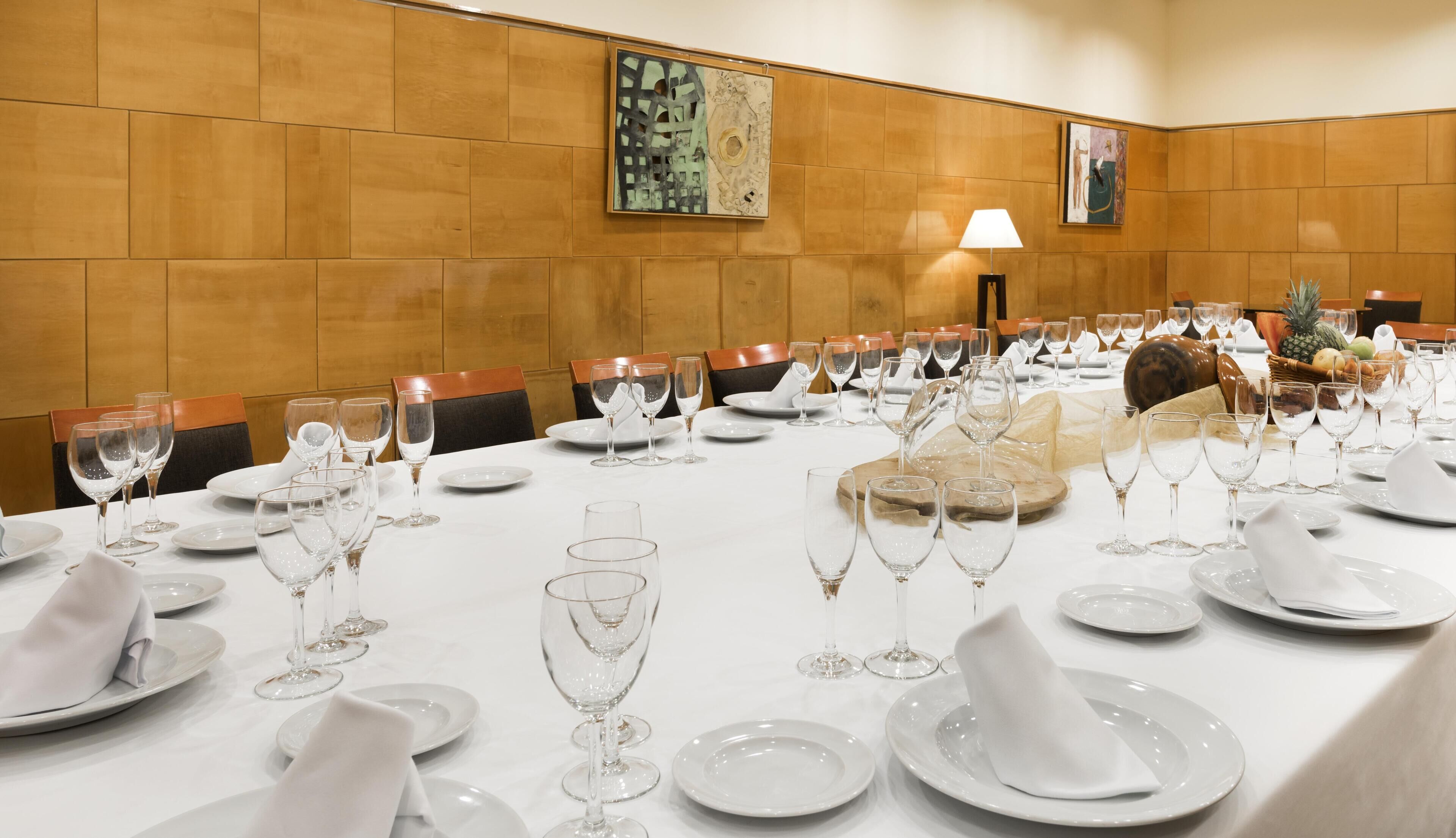 A conference room with a long table set for a meeting, equipped with chairs, plates, and wine glasses.
