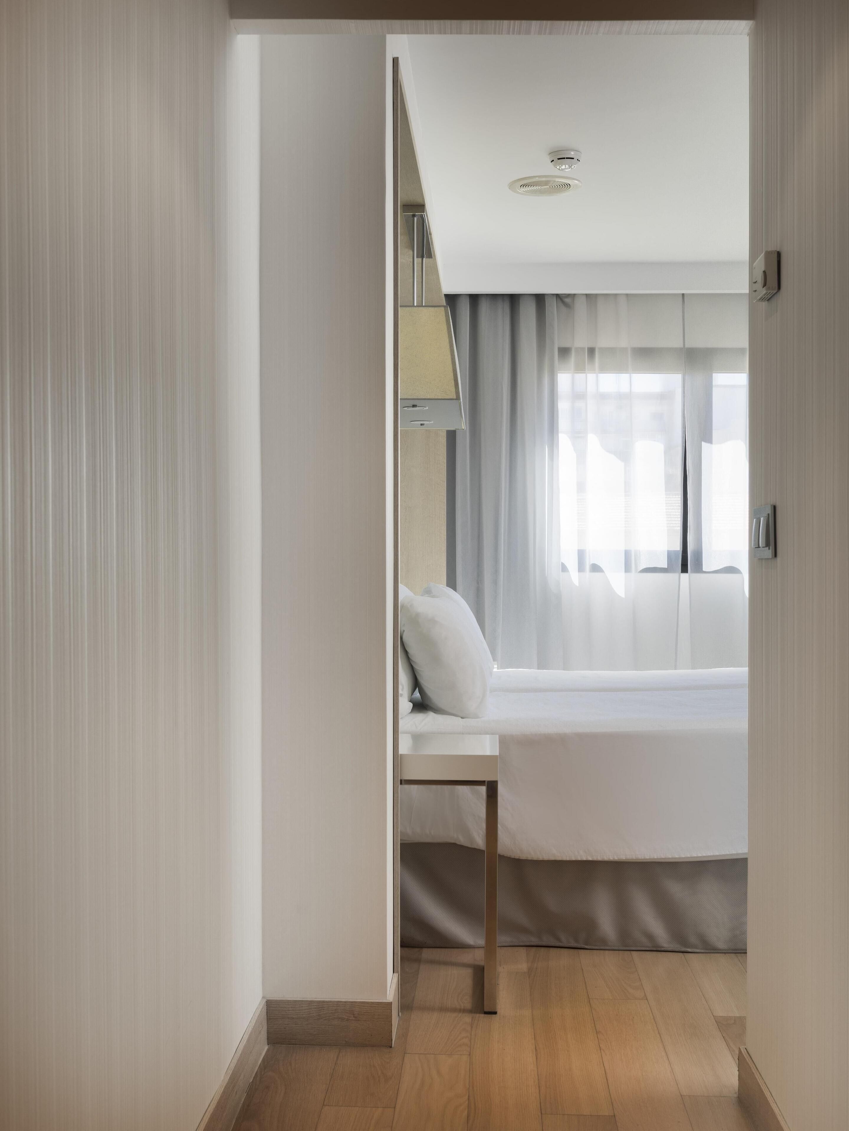 A bedroom with a bed, a bedside table, a lamp, and a window with curtains.