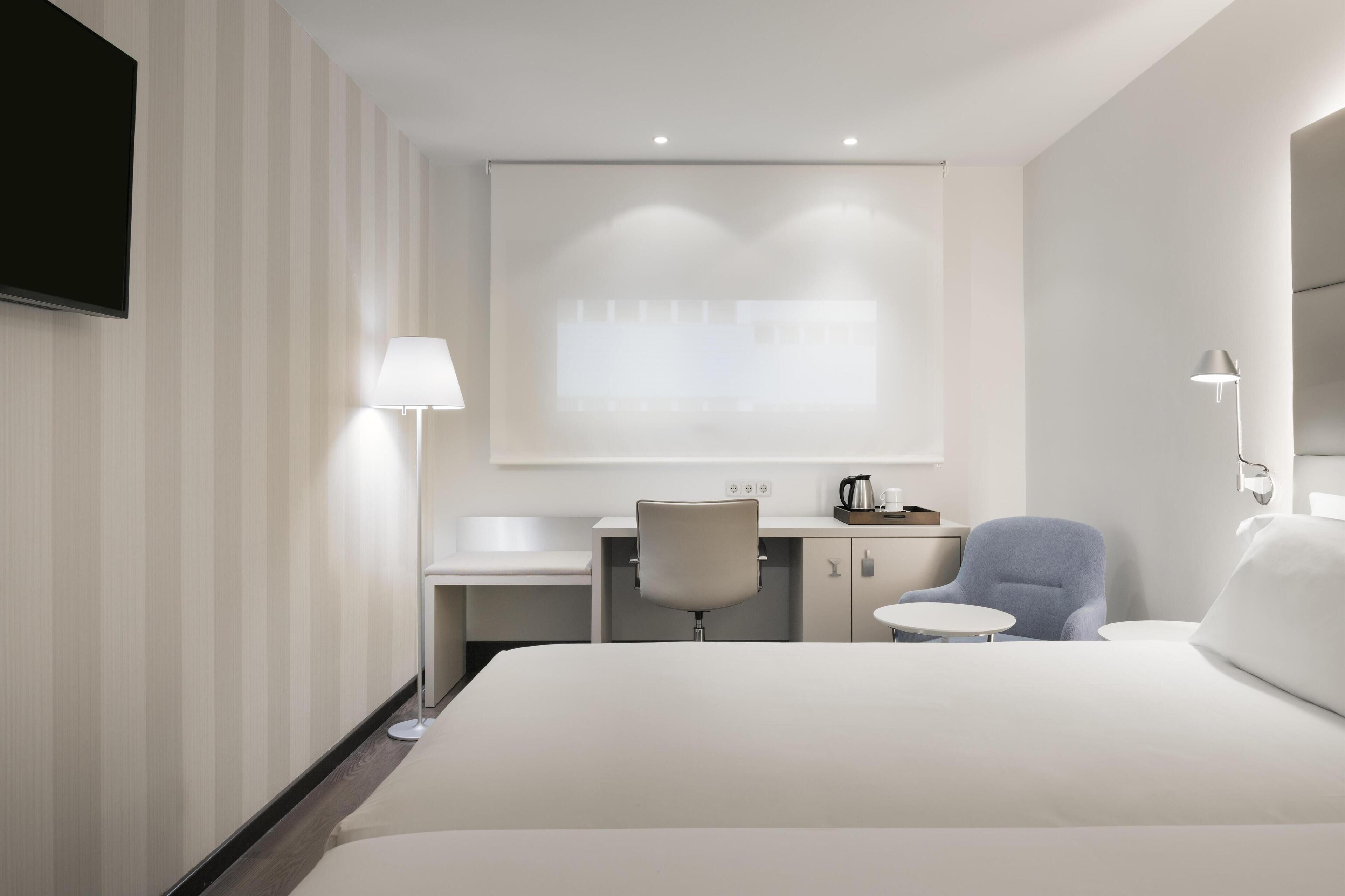 A modern hotel room with a bed, desk, chair, and a flat-screen TV mounted on the wall.