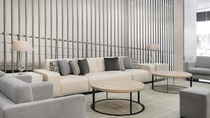 A modern lounge area with a sofa set, two round tables, and a decorative wall with vertical lines. - NH Ciudad Real (Ciudad Real)