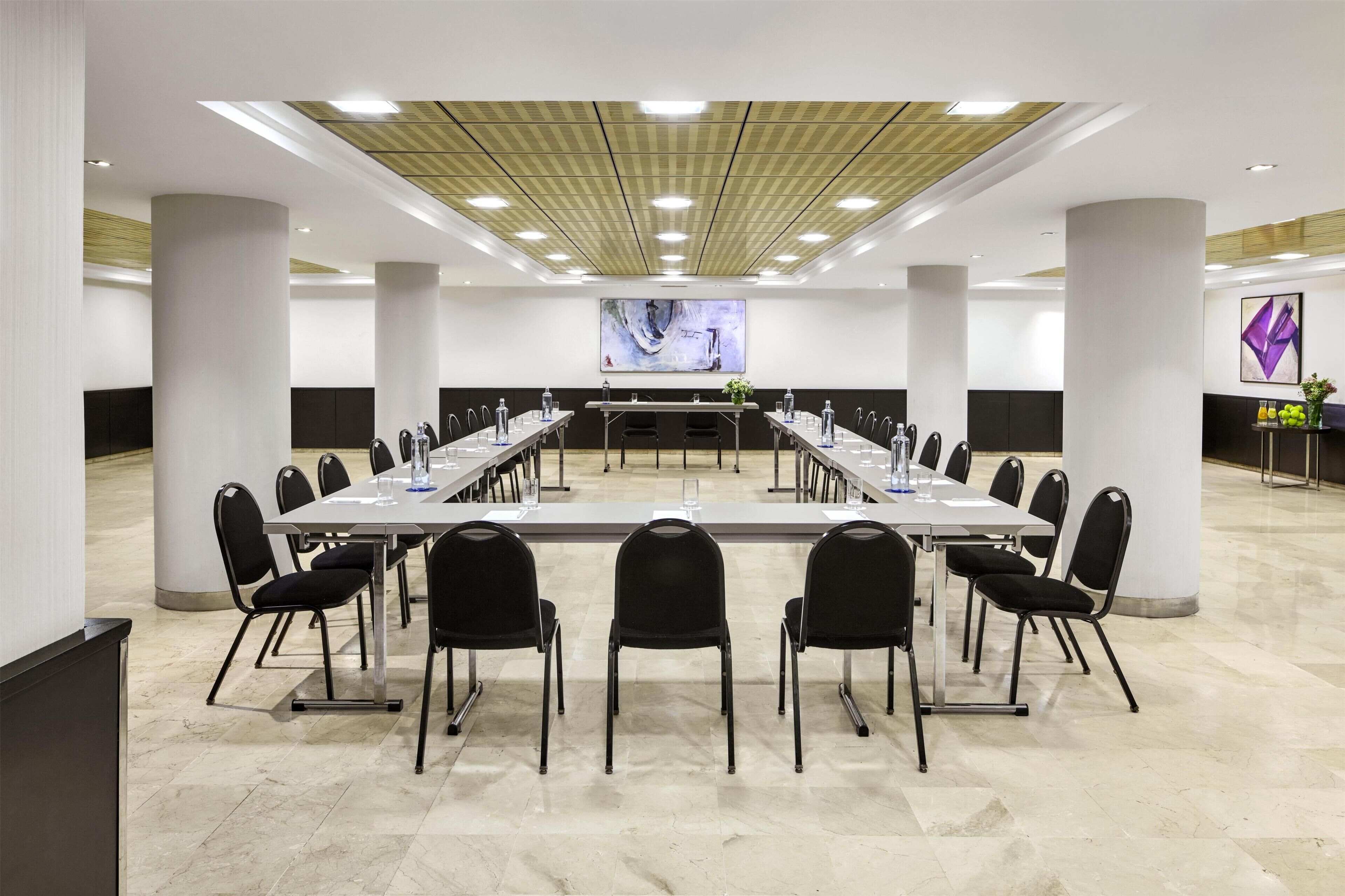 Un salón de conferencias con una larga mesa, sillas y una pantalla grande al frente.