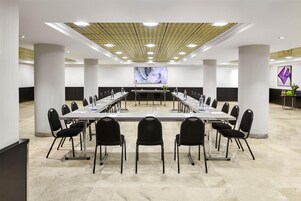 Un salón de conferencias con una larga mesa, sillas y una pantalla grande al frente.