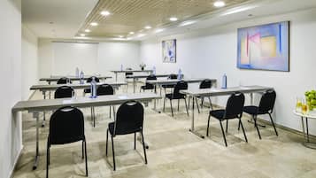 Una sala de conferencias con varias mesas y sillas, una pantalla de proyector y obras de arte en las paredes.